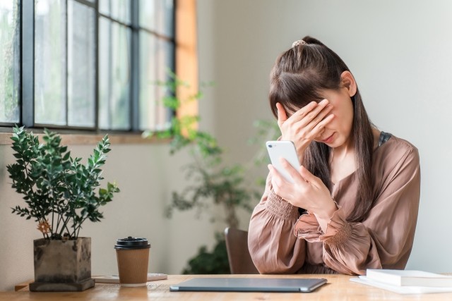 カフェでスマホを見てショックを受ける女性