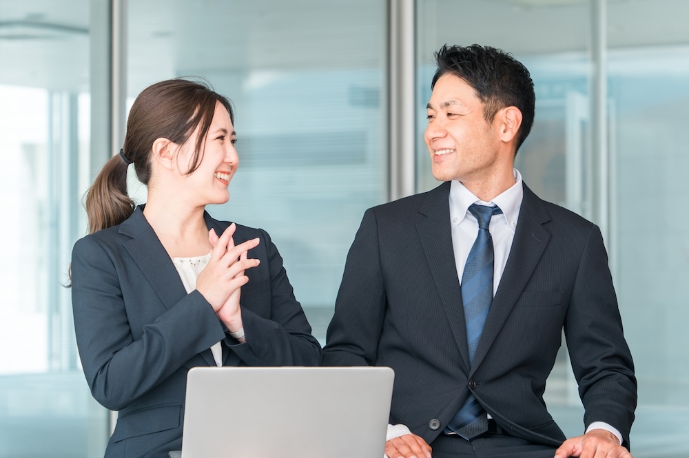 職場で笑顔で話し合う男女の画像