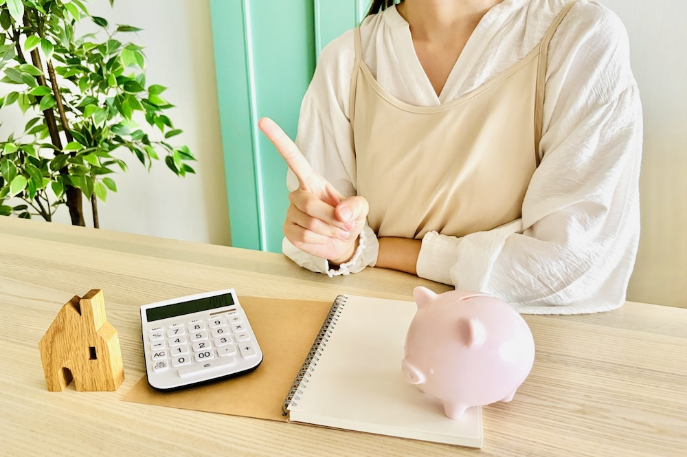 女性が貯金箱と電卓の置かれたテーブルで教えている様子の画像