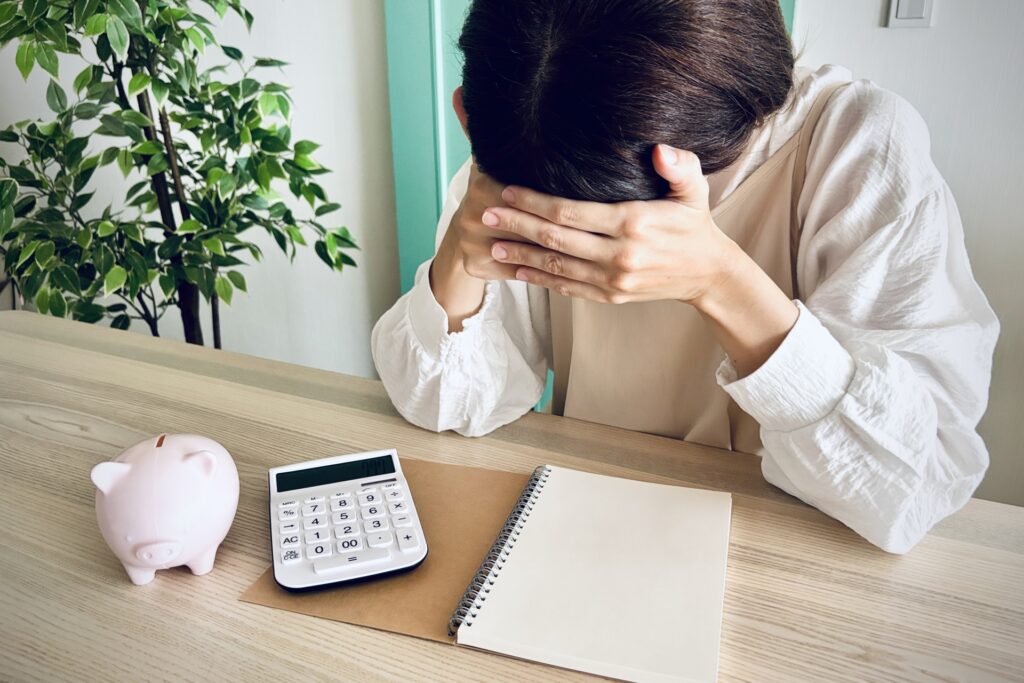 電卓と貯金箱を前に頭を抱える女性