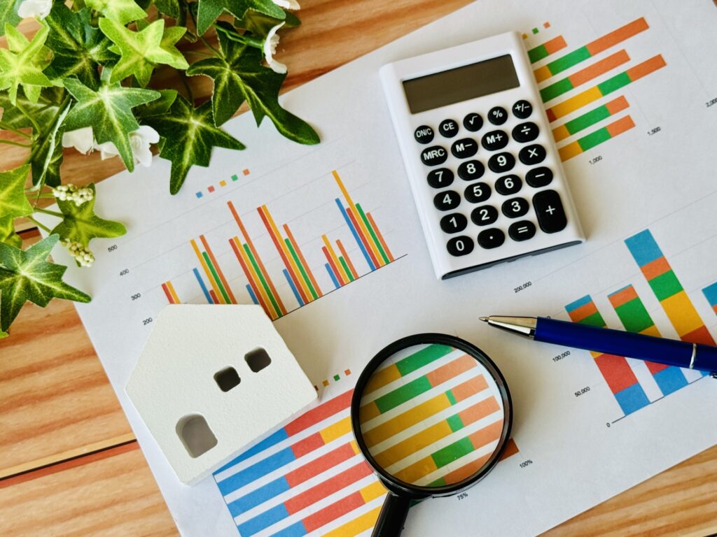 グラフの書かれた紙に置かれた電卓、虫眼鏡、ペン